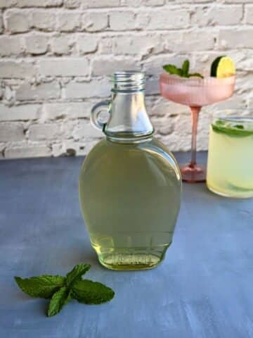 a bottle of mint simple syrup with cocktails in the background