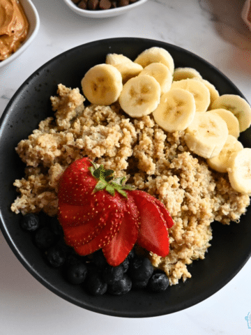 a bowl of breakfast quinoa cooked in a slow cooker topped with sliced bananas and strawberries