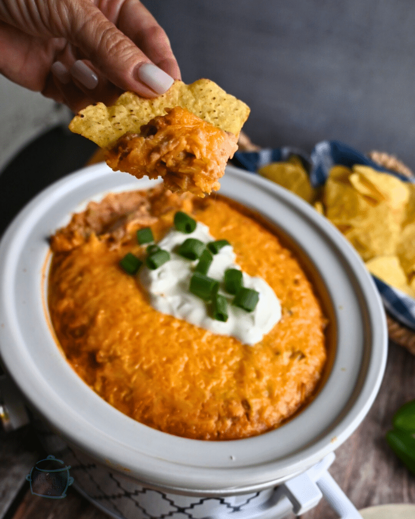 Texas trash dip being scooped up out of a slow cooker onto a tortilla chip