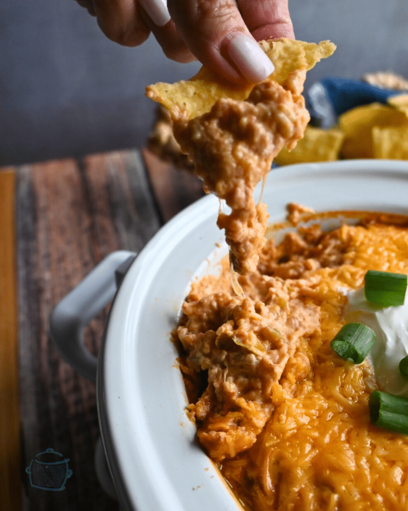 Texas trash dip being scooped up out of a slow cooker onto a tortilla chip