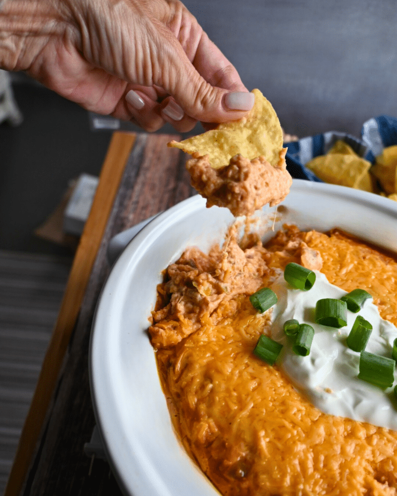 Texas trash dip being scooped up out of a slow cooker onto a tortilla chip