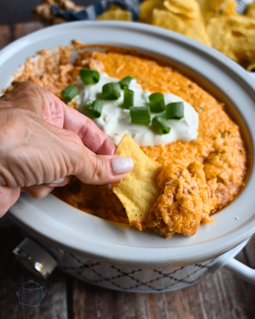 Texas trash dip being scooped up out of a slow cooker onto a tortilla chip