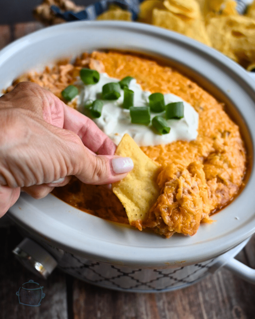 Texas trash dip being scooped up out of a slow cooker onto a tortilla chip