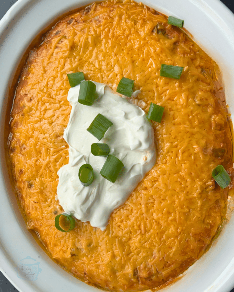 an oval slow cooker filled with cooked Texas trash dip topped with sour cream and green onion