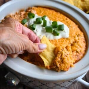 Texas trash dip being scooped up out of a slow cooker onto a tortilla chip