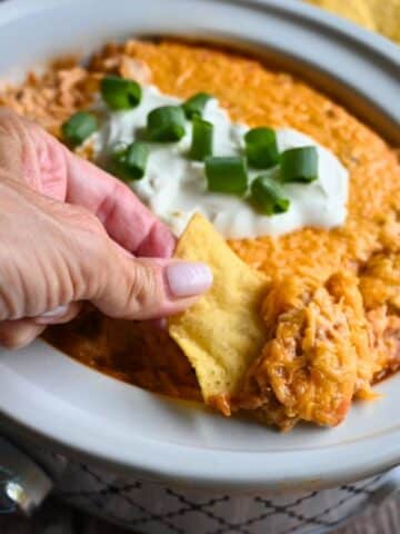 Texas trash dip being scooped up out of a slow cooker onto a tortilla chip