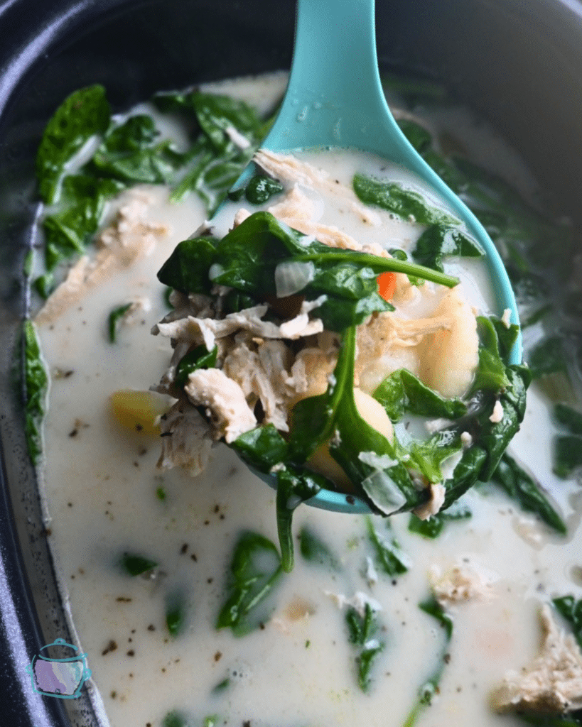 creamy chicken gnocchi soup on a ladle held over a slow cooker.