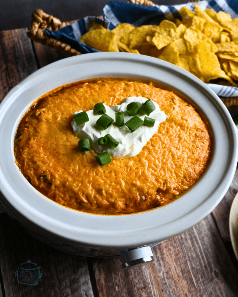 an oval slow cooker filled with cooked Texas trash dip topped with sour cream and green onion.