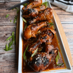 a white rectangular tray with a row of Korean spicy drumsticks