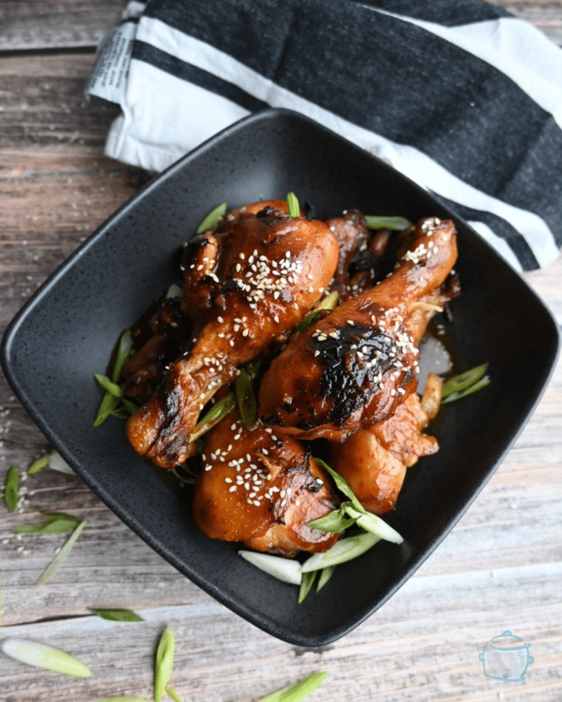Cooked and crisped drumsticks in a black square bowl.