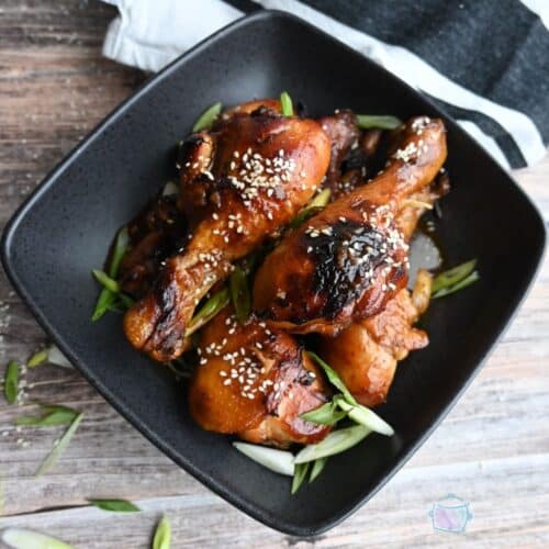 Cooked and crisped drumsticks in a black square bowl.