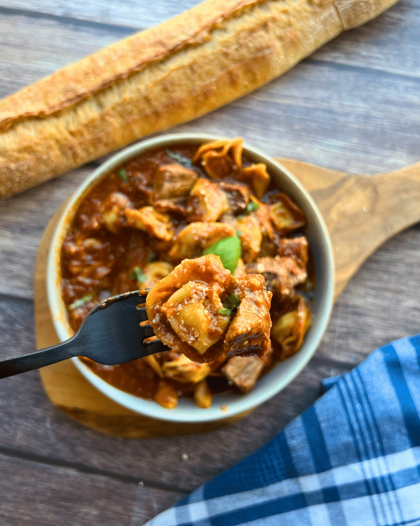 Slow Cooker Beef and Tortellini with red sauce in a round grey bowl.