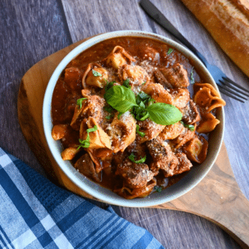 Slow Cooker Beef and Tortellini with red sauce in a round grey bowl.