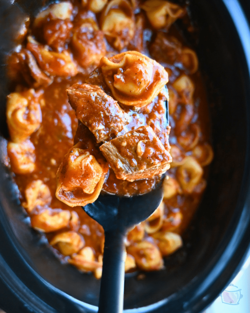 Beef and tortellini on a spoon over a slow cooker