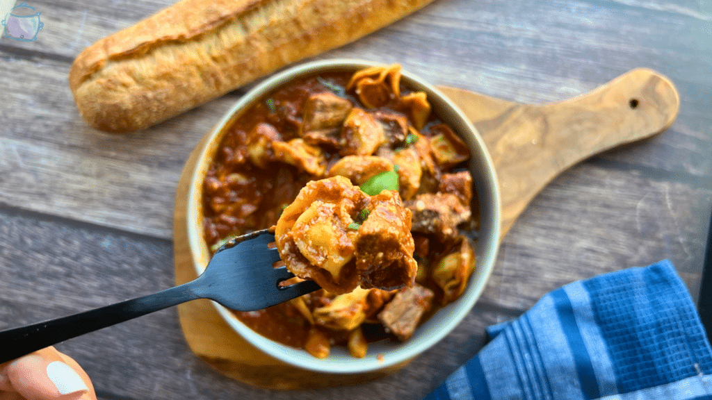 Slow Cooker Beef and Tortellini with red sauce in a round grey bowl.