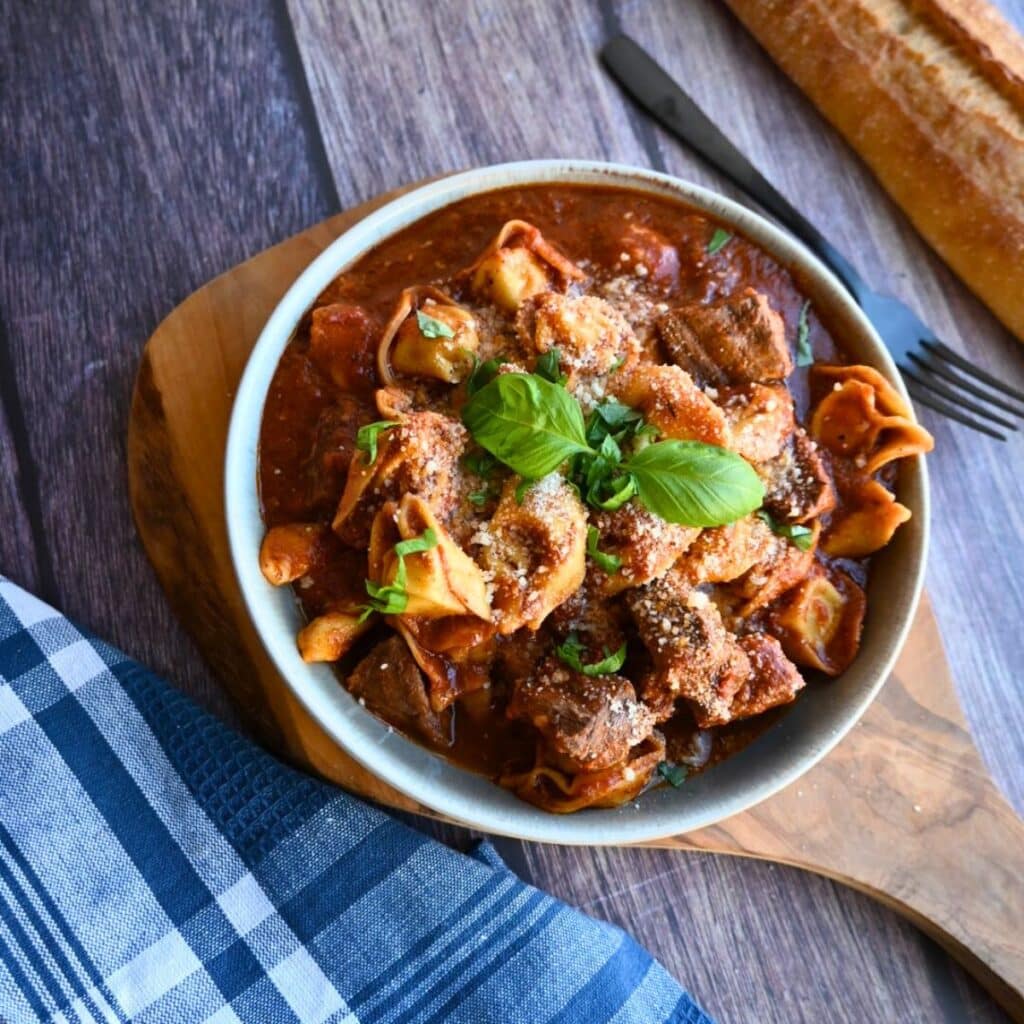 Slow Cooker Beef and Tortellini with red sauce in a round grey bowl.