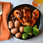 sliced turkey breast on a round black plate with potatoes and broccoli