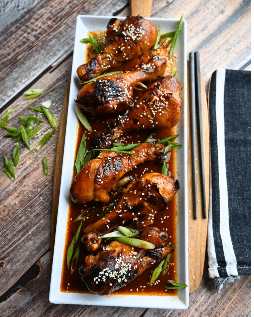 a white rectangular tray with a row of Korean spicy drumsticks