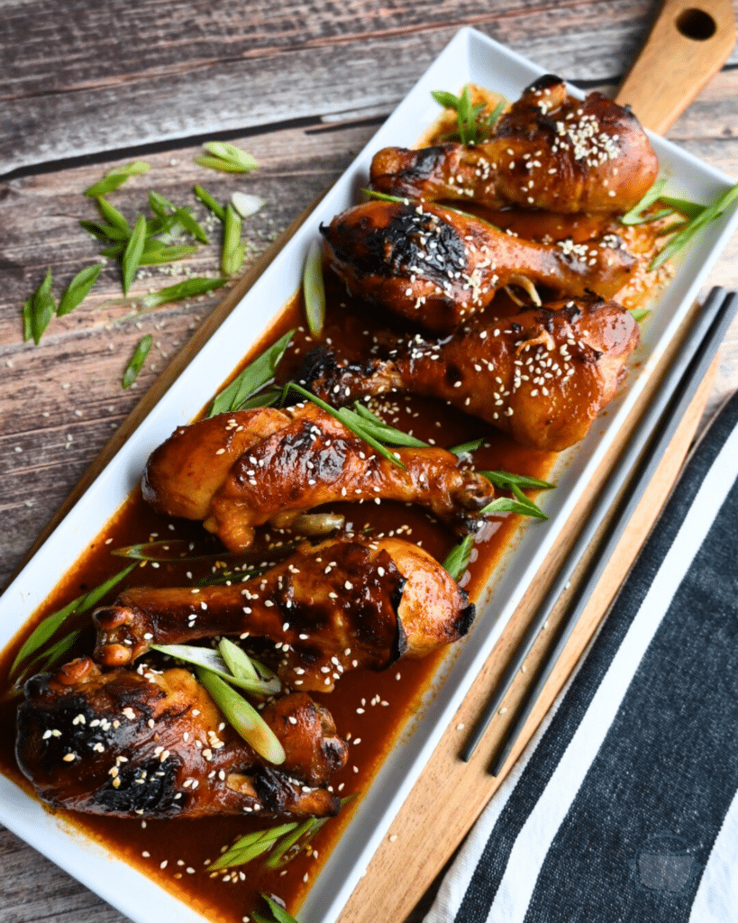a white rectangular tray with a row of Korean spicy drumsticks
