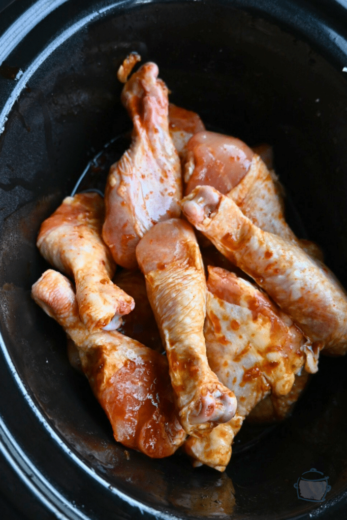 drumsticks covered in Korean spicy sauce in slow cooker before cooking.