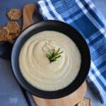 parsnip soup in a black bowl with a sprig of rosemary on top