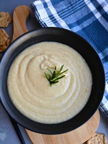 parsnip soup in a black bowl with a sprig of rosemary on top