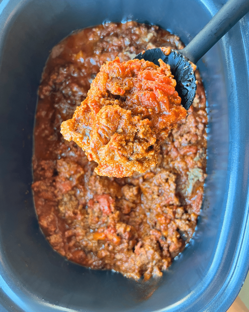 cooked taco meat on a spoon over a slow cooker filled with the same.