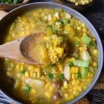 pepper and corn chowder in a round gray bowl with a wooden spoon.