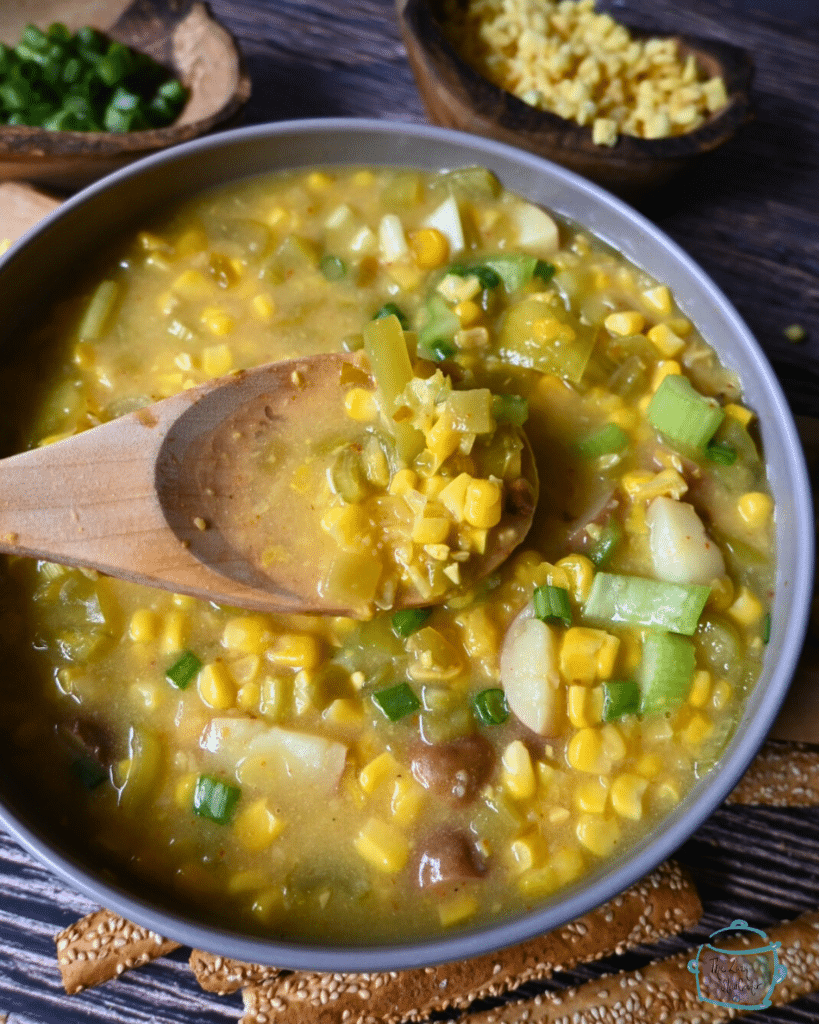 pepper and corn chowder in a round gray bowl with a wooden spoon.