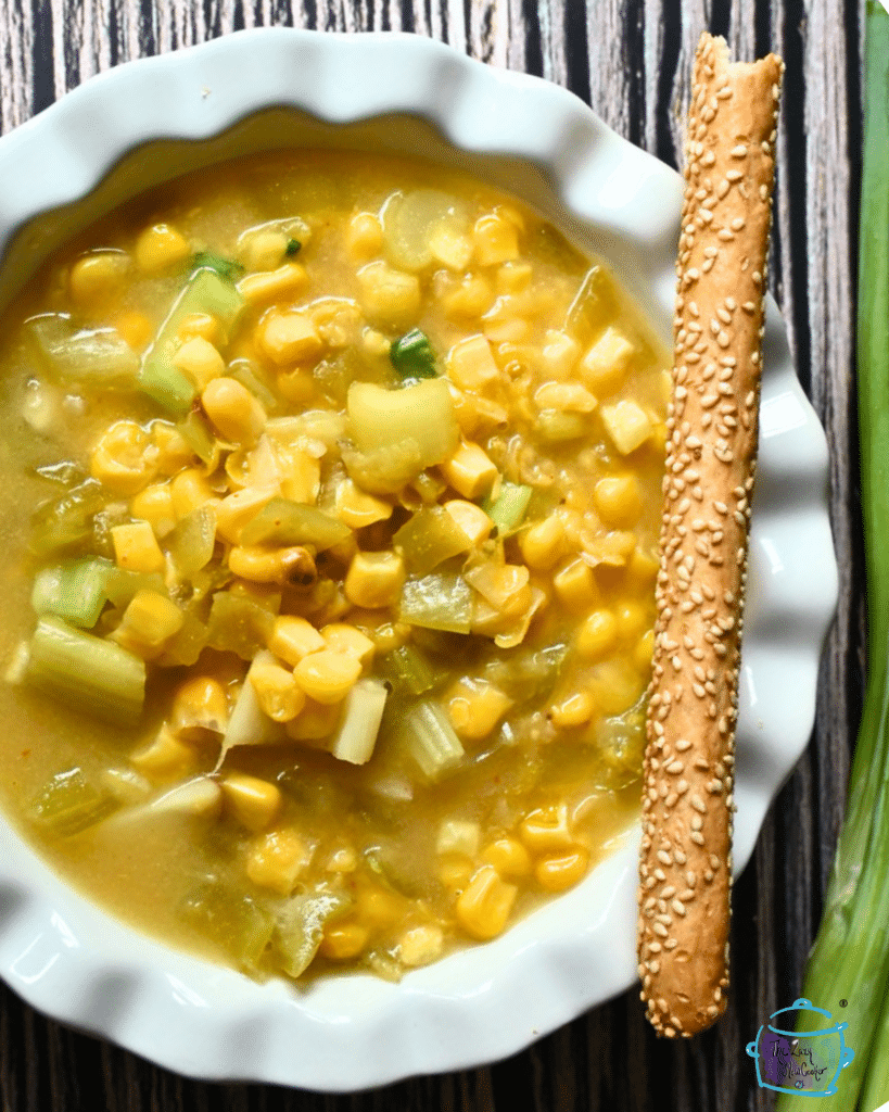 vegan corn chowder in white bowl with a bread stick on the side
