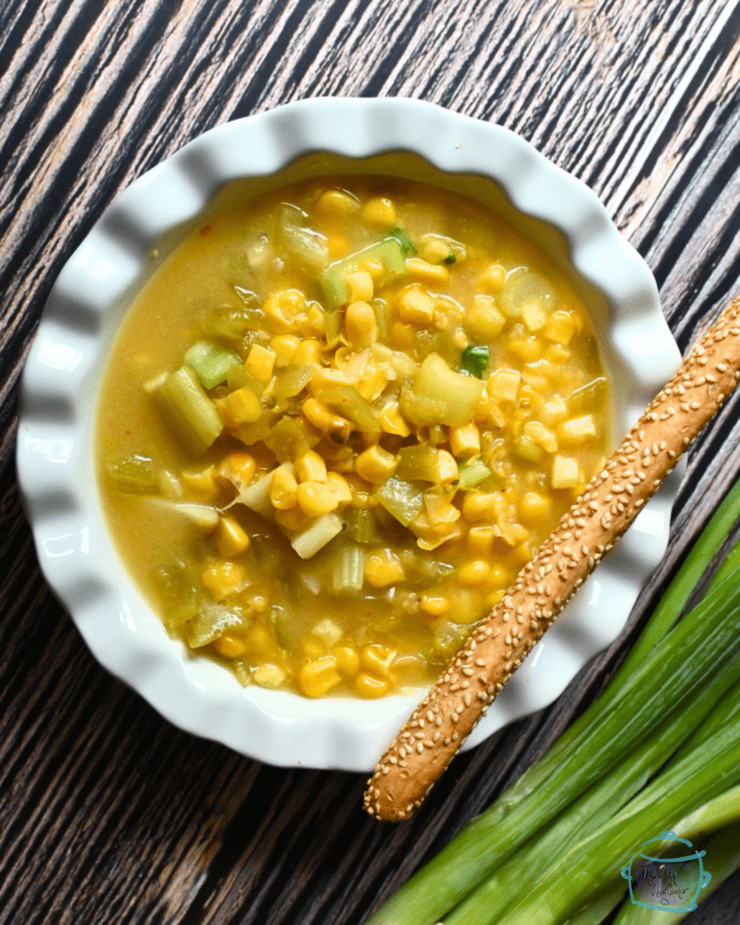vegan corn chowder in white bowl with a bread stick on the side
