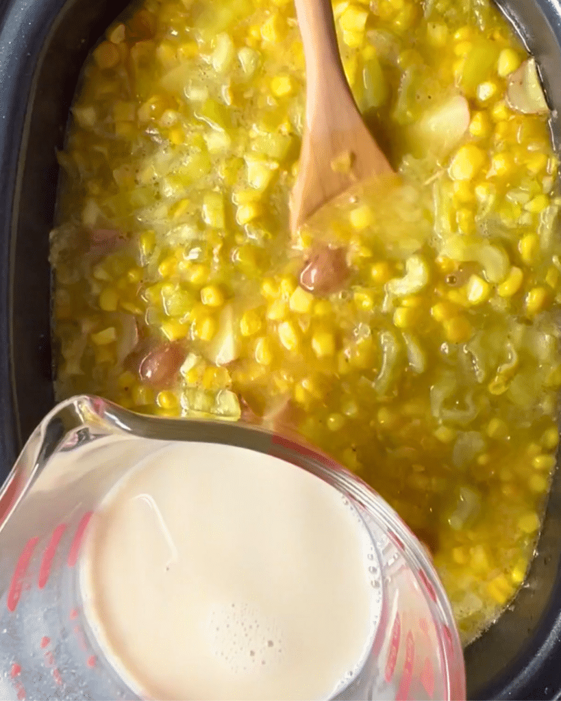 Adding oatmilk to a slow cooker filled with began pepper and corn chowder