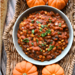 a bowl of vegetarian pumpkin chili surrounded by mini pumpkins