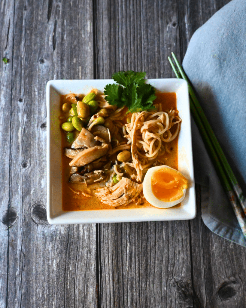 Thai curry ramen with chicken in a square bowl with an egg on the side