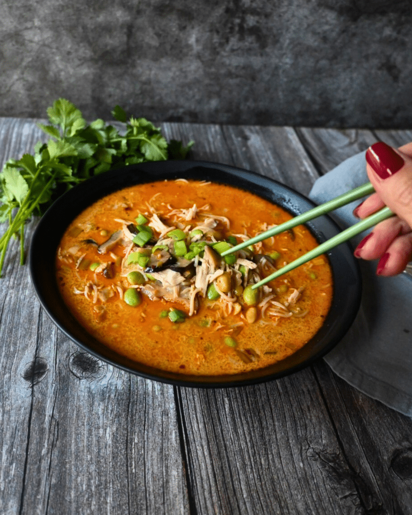 a black bowl filled with coconut Thai curry ramen with chicken and chopsticks