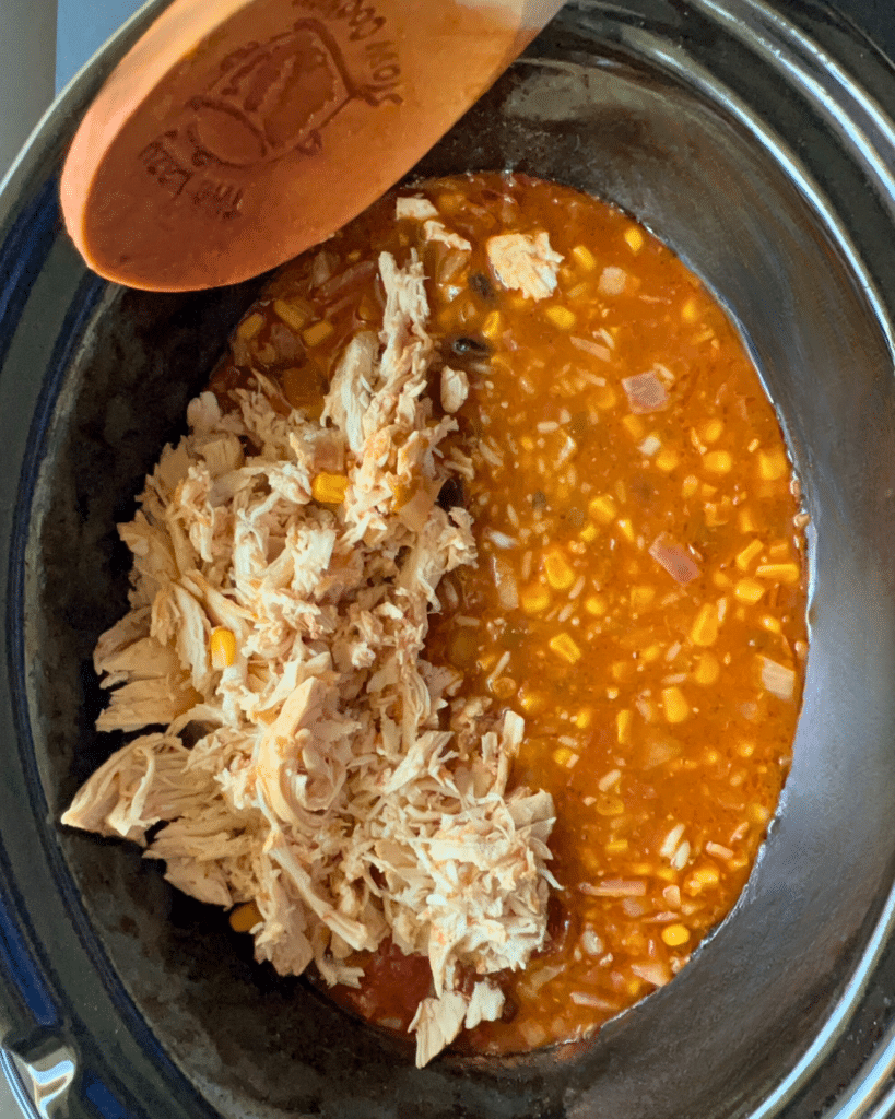 shredded chicken being added to a slow cooker