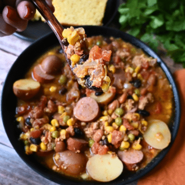 Texas cowboy stew in a black bowl with cornbread on the side