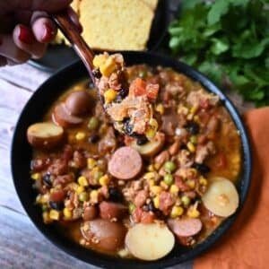 Texas cowboy stew in a black bowl with cornbread on the side