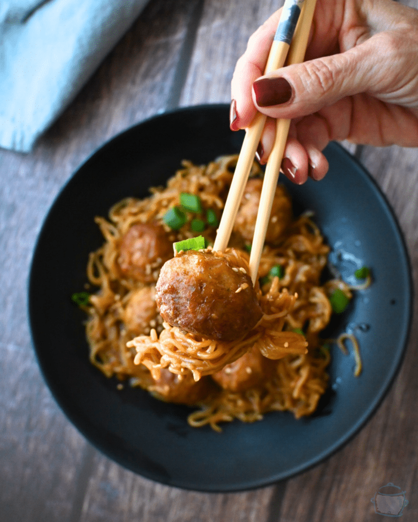 a bowl full of slow cooker meatballs and ramen with chopsticks