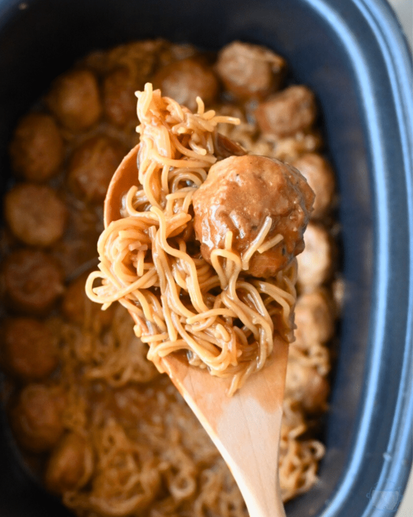 Ramen and meatballs in a Mongolian inspired sauce on a wooden spoon over a crockpot full of the same.