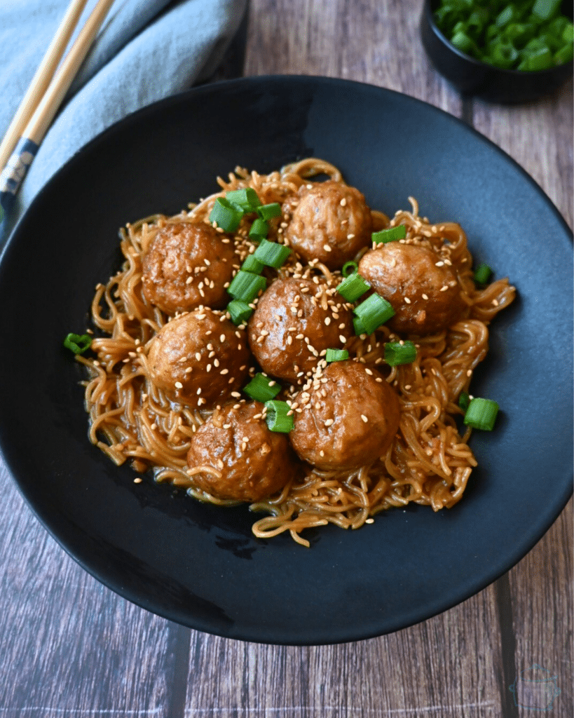a bowl full of slow cooker meatballs and ramen with chopsticks