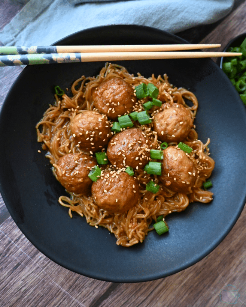 a bowl full of slow cooker meatballs and ramen with chopsticks