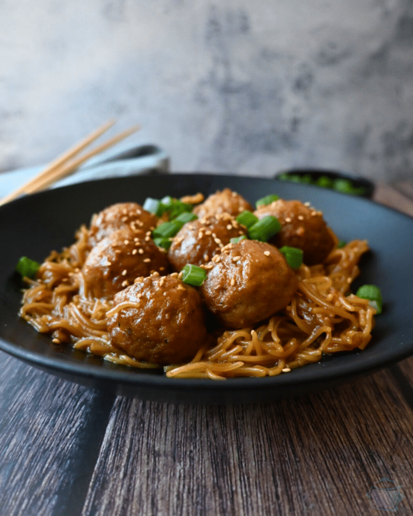 a bowl full of slow cooker meatballs and ramen with chopsticks