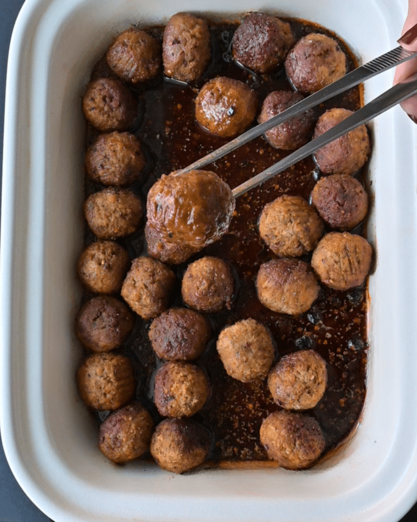 a meatball held over a slow cooker full of the same