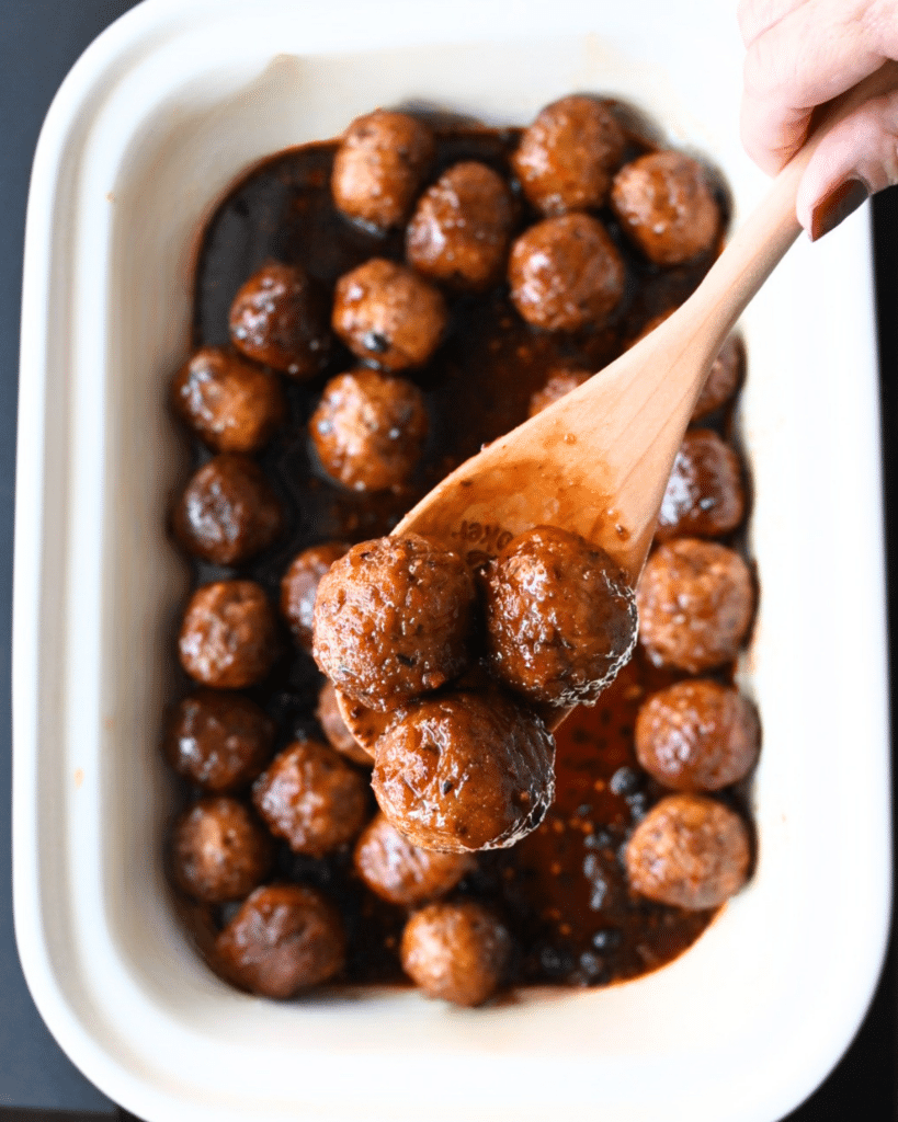 meatballs on a wooden spoon held over a crockpot full of the same