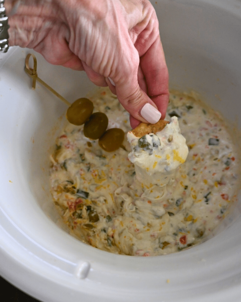 slow cooker dirty martini dip on a cracker over a slow cooker of the same