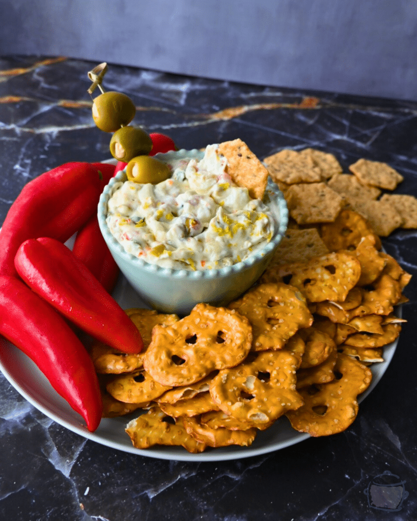 Dirty martini slow cooker dip in a bowl in the middle of pretzels crackers and peppers