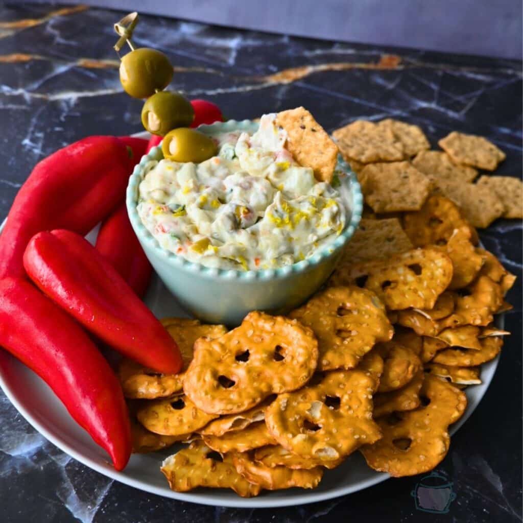 Dirty martini slow cooker dip in a bowl in the middle of pretzels crackers and peppers