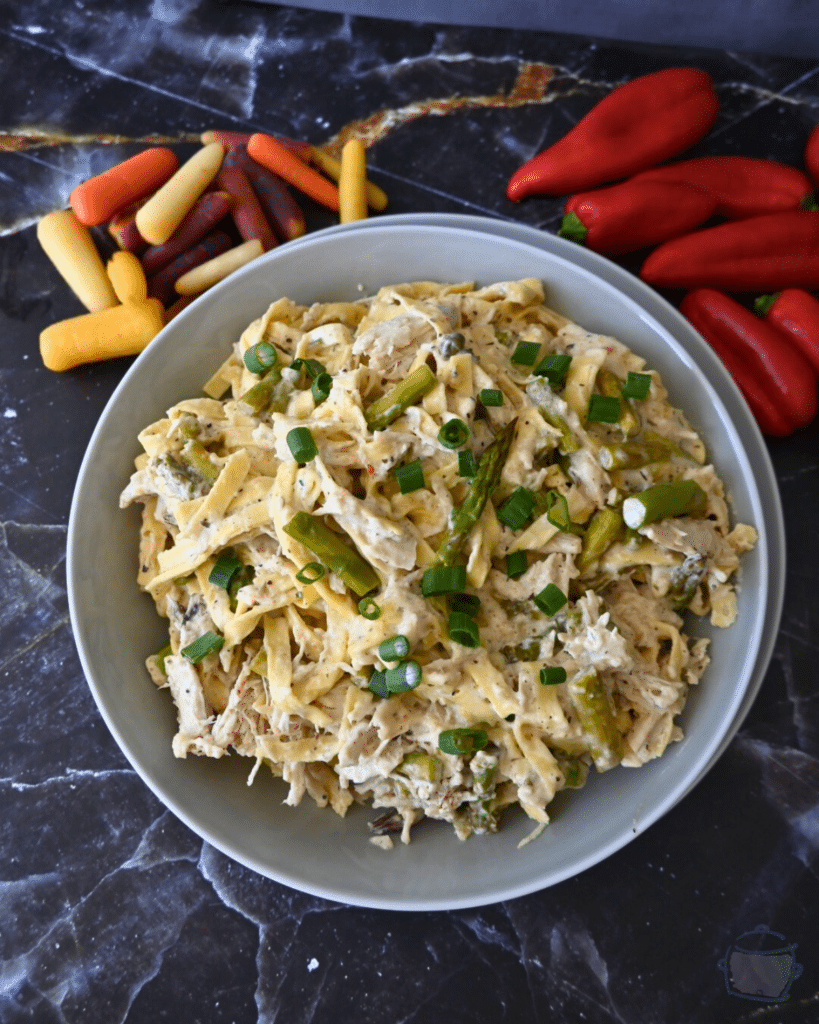 a bowl full of slow cooker caesar chicken pasta with veggies in the background