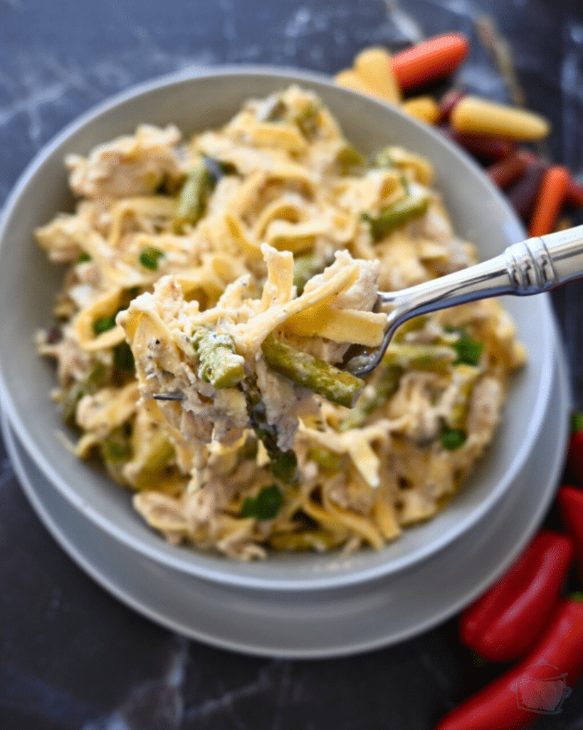 a bowl full of slow cooker caesar chicken pasta some is held up on a fork
